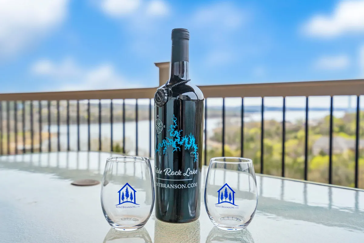 A private deck or balcony with a bottle of wine and two glasses arranged on a table, overlooking the sparkling lake. The view is peaceful and ideal for enjoying coffee in the morning or drinks at sunset, with the water and shoreline in the background.
