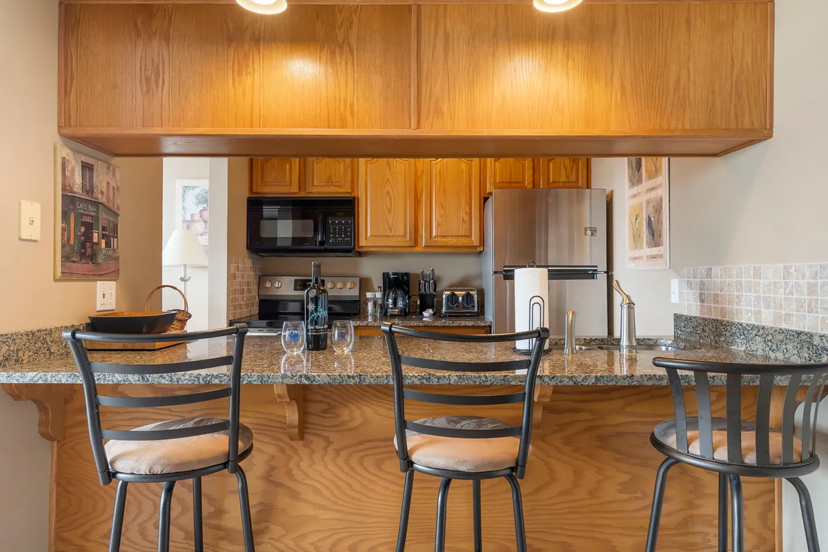 This interior shot highlights a bar counter, kitchen appliances, and wine glasses, creating an atmosphere suited for both cooking and entertaining. The scene suggests casual dining and social gatherings, emphasizing the kitchen's open, inclusive design.