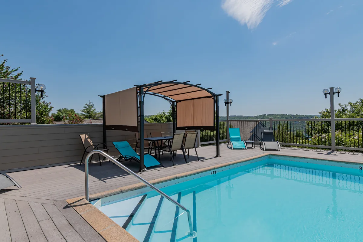 An inviting outdoor pool area with a sparkling swimming pool, canopy-covered seating, comfortable lounge chairs, and lush greenery. The pool is a hub of activity during the summer and offers a relaxing place to socialize or unwind.