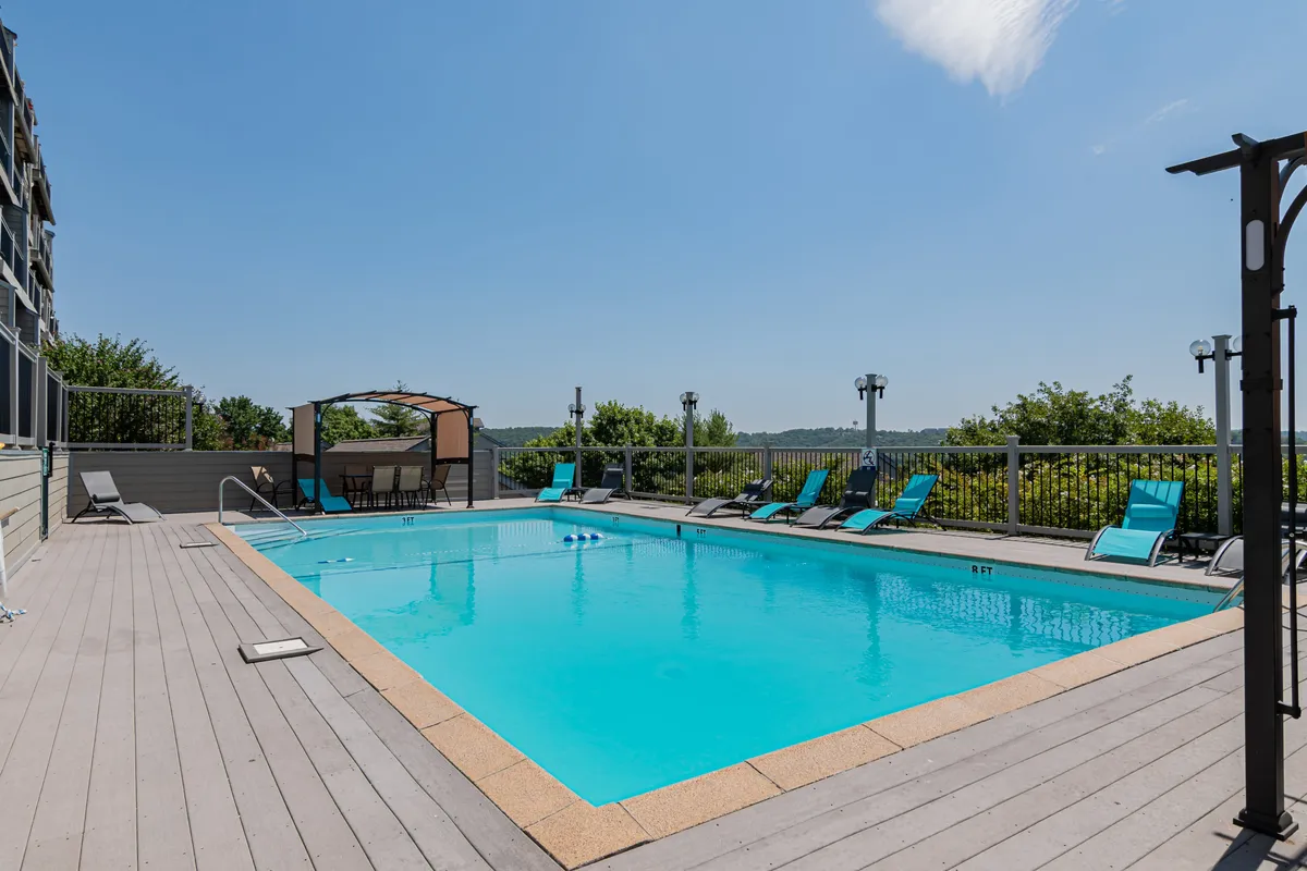 The image features an inviting outdoor swimming pool, surrounded by comfortable lounge chairs and a canopy seating area. The serene pool space is designed for relaxation and social gatherings, with greenery creating a tranquil backdrop. The setting captures the essence of resort-style leisure.