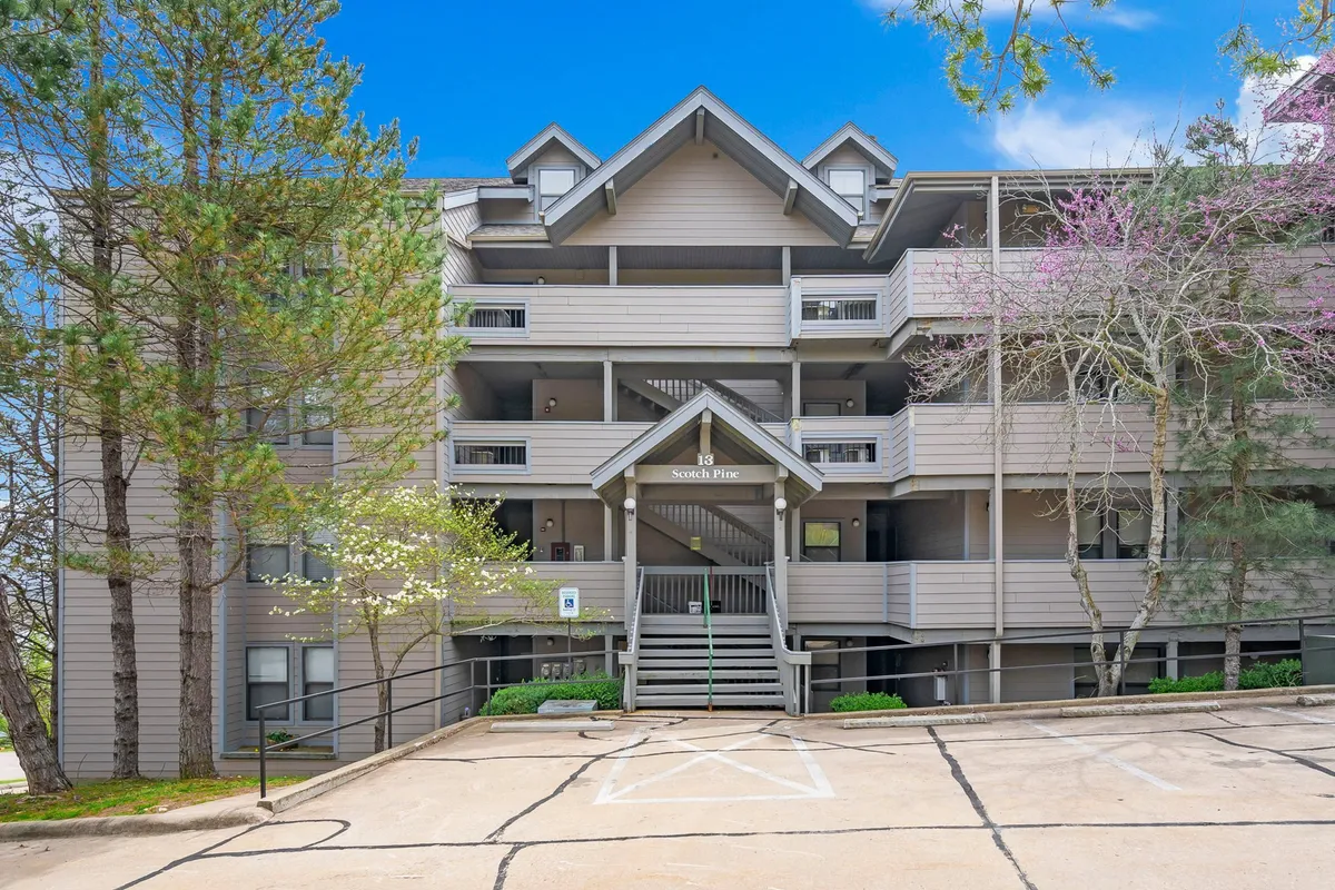 The exterior shot shows the entrance of a residential building surrounded by mature trees and balconies that overlook the greenery. The tranquil atmosphere invites guests to relax outdoors or enjoy the serene view from their private decks—ideal after a day of teeing off or exploring.
